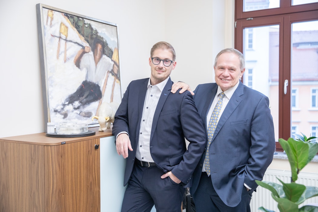 In einem hellen Raum hängt an der linken Wand ein Bild, daneben stehen Constantin Behr (Junior) und Herbert Behr (Senior). Sie sind die Gründer der Golden Gates AG.
