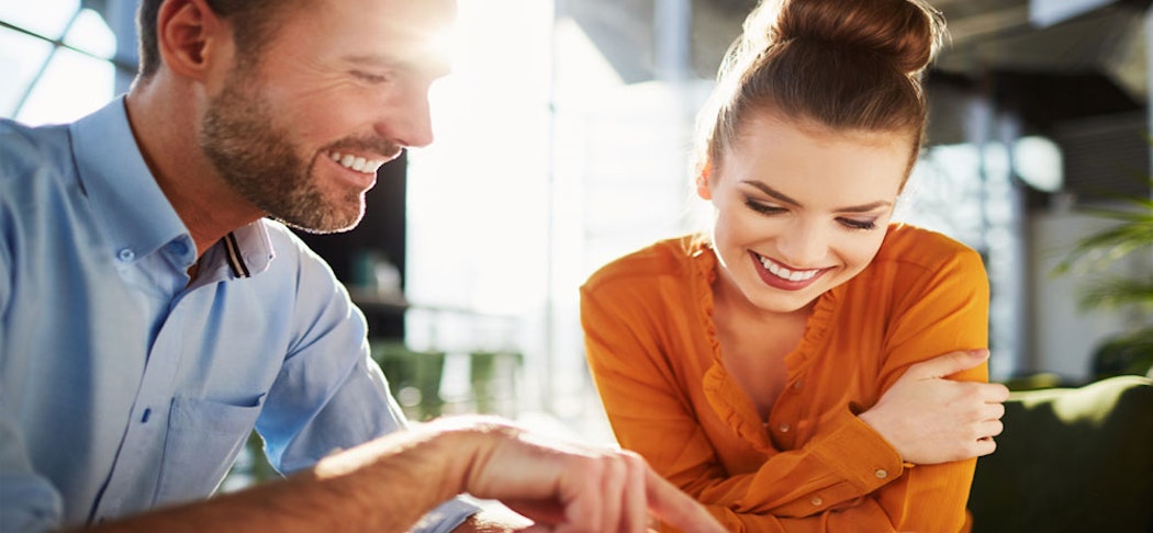 In einem hell beleuchteten großen Raum, beugen sich ein Mann und eine Frau über ein Smartphone und melden sich bei den informativen Seminaren und Veranstaltungen von der Golden Gates AG an.